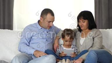 一家人坐在沙发上，全神贯注地看着平板电脑屏幕。 爸爸，妈妈，<strong>还有</strong>一个小孩